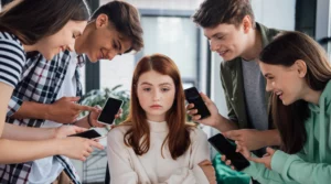 grupo de jovens caçoando de uma menina com celulares na mã